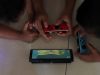 Two children playing a handheld game console propped on a tiled floor