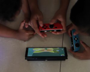 Two children playing a handheld game console propped on a tiled floor