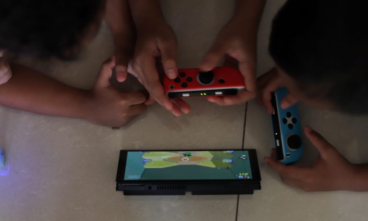 Two children playing a handheld game console propped on a tiled floor