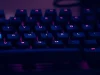 A backlit computer keyboard glowing purple in a dark room