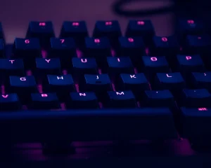 A backlit computer keyboard glowing purple in a dark room