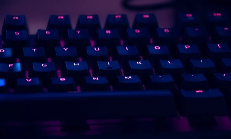 A backlit computer keyboard glowing purple in a dark room